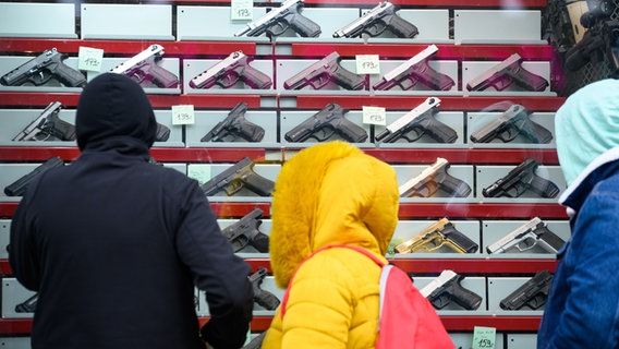 People stand in front of the display of a gun shop that sells alarm and signal weapons. © dpa
